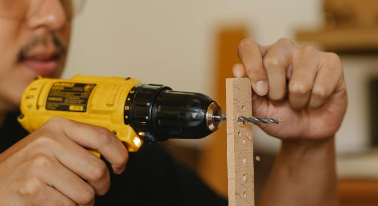 Crop anonymous male with mustache using drill while working with timber detail in workshop